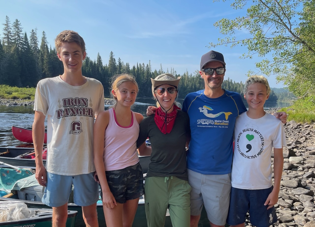Family on the shore of the Allagash River, Maine, with canoes